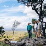 Three people standing on a rock edge looking over Arcadia Valley, Queensland