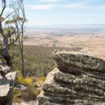 A guest sitting on a rocky surface, holding her hat on her head
