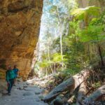 Two people walking underneath a rocky structure