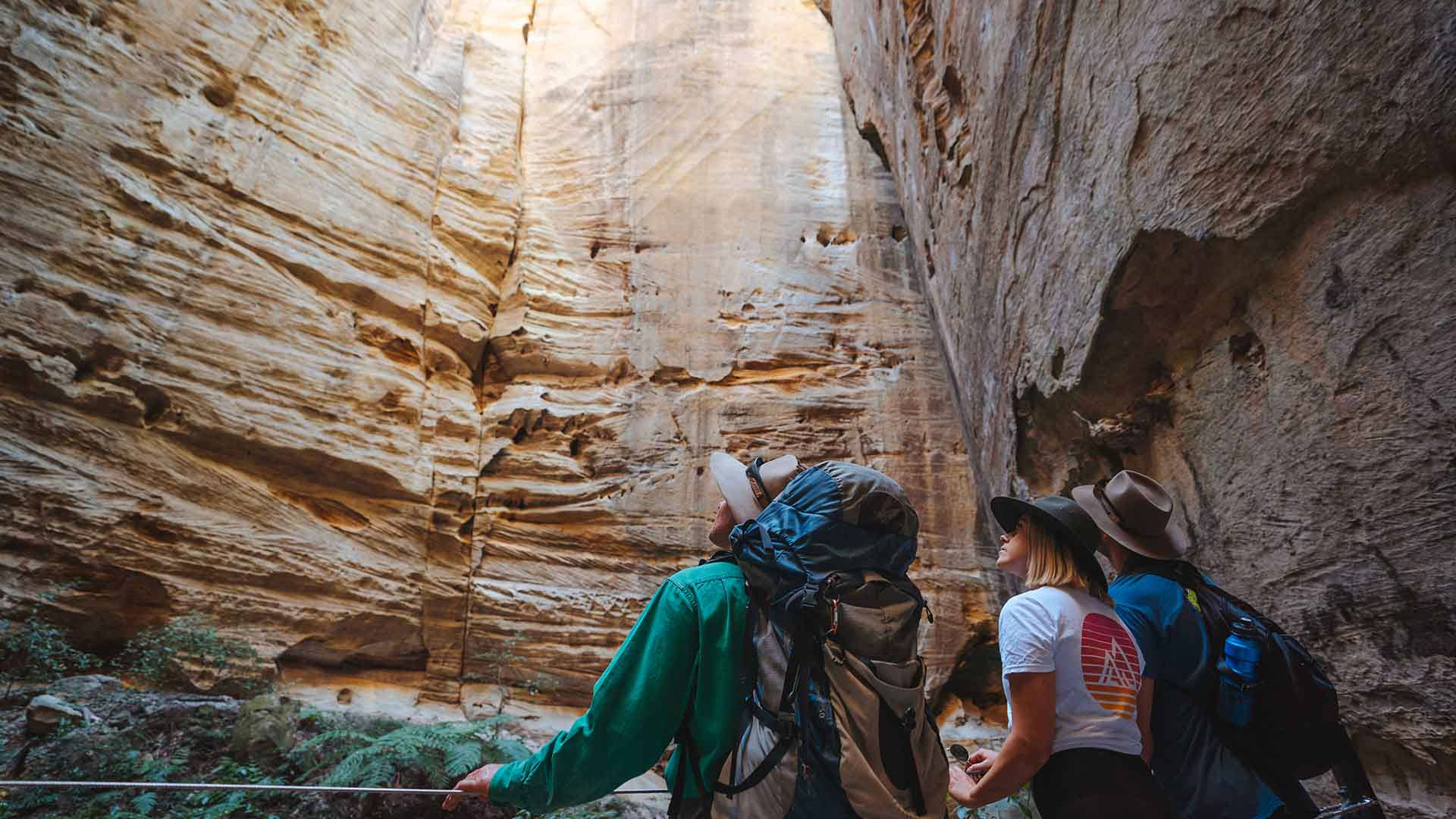 Three people looking up towards an opening in a cave