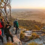 A group of people standing at the edge of a cliff looking out to the valley below