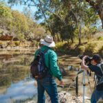 A man standing next to another man taking a photo of the river