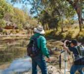 A man standing next to another man taking a photo of the river