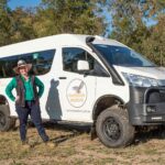 Rose Aisthorpe posing besides a white 4WD tour bus